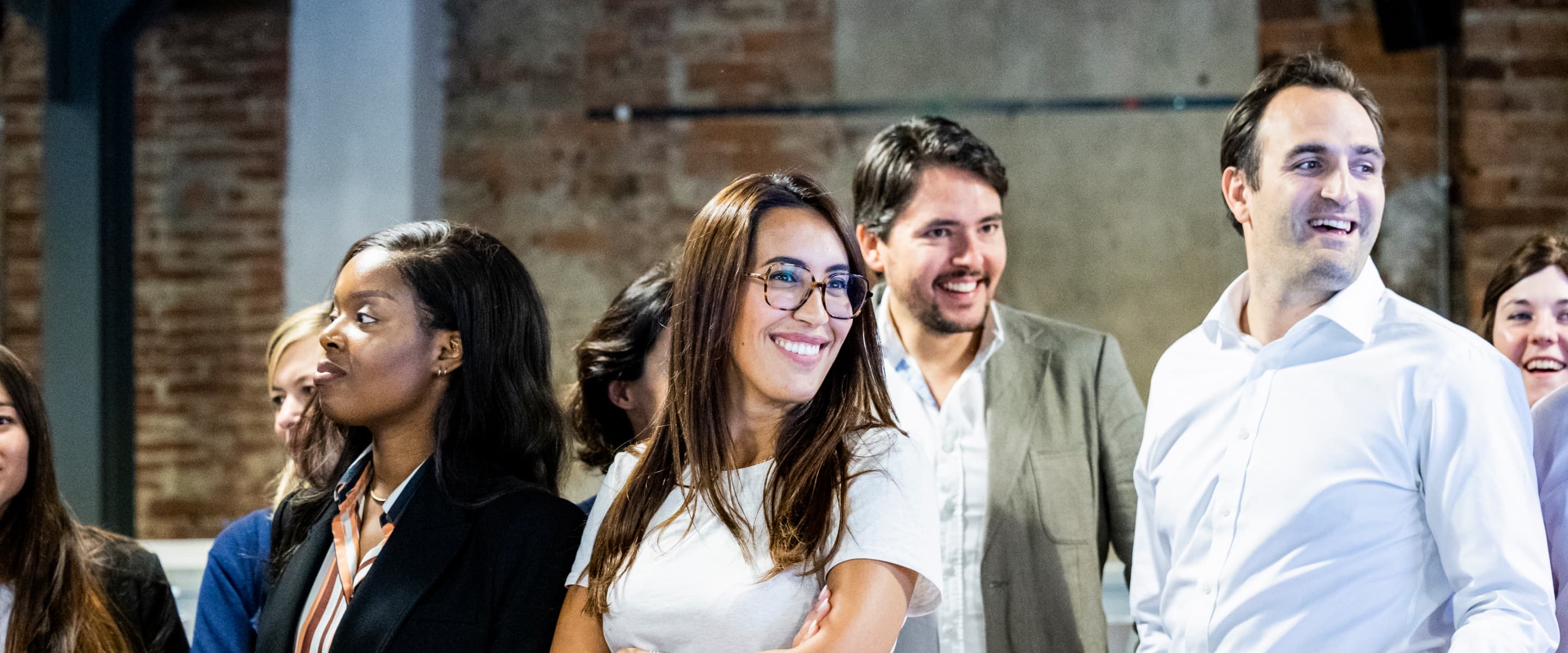 A diverse group of people in business attire stand together, smiling and looking in various directions.