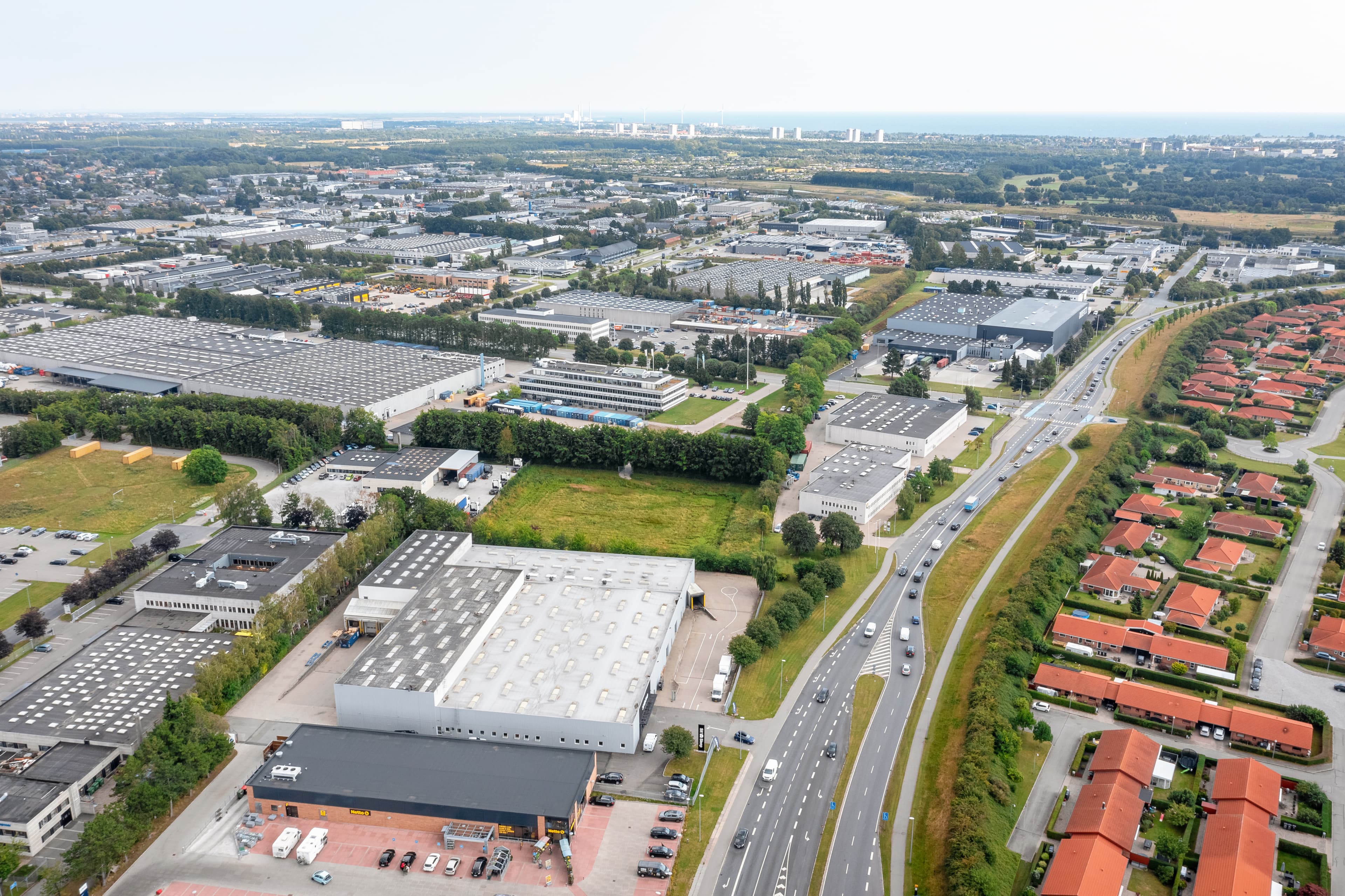 Aerial view of an industrial area with warehouses, roads, and residential buildings under a clear sky.
