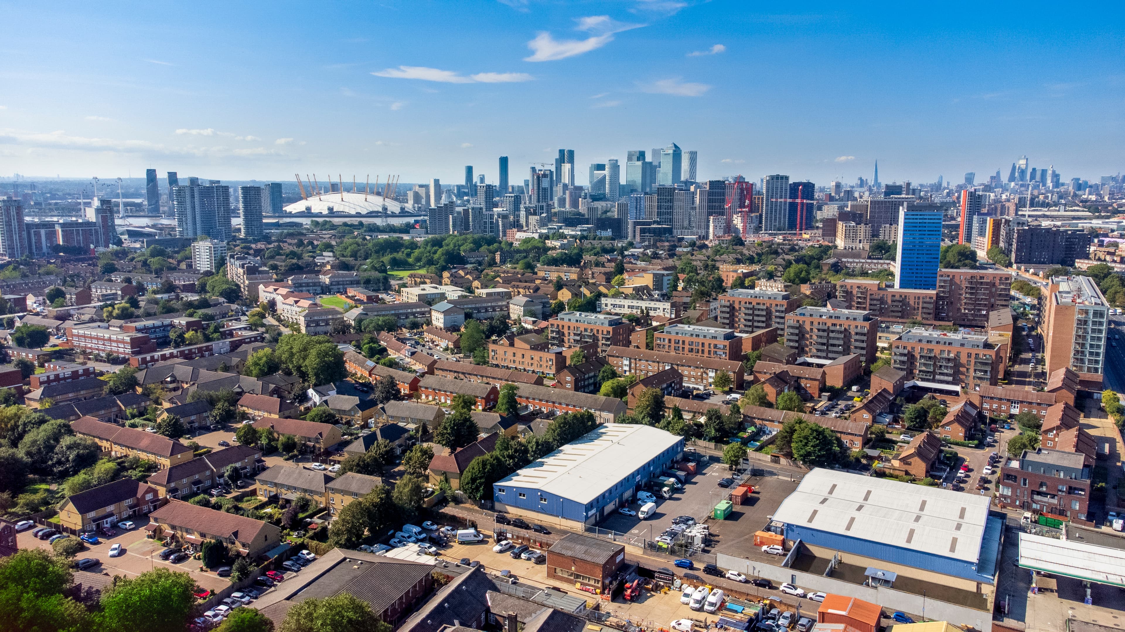 Aerial view of a cityscape featuring residential buildings in the foreground and a modern skyline, including a large dome structure, in the background under a clear blue sky.