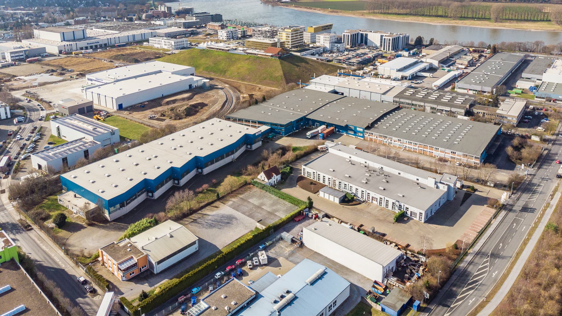 Aerial view of an industrial area with several large warehouses, roads, and a river in the background.