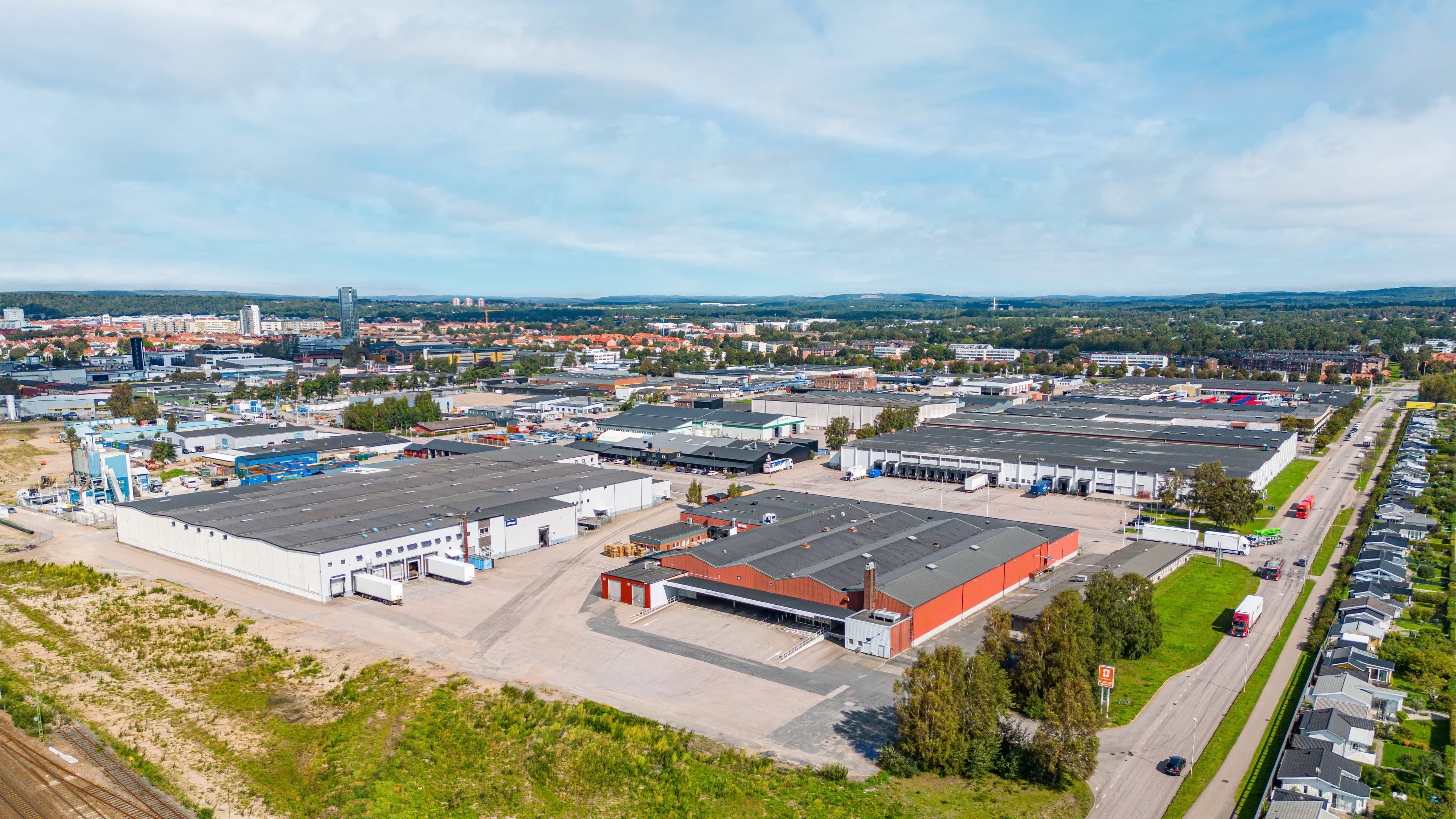 Aerial view of an industrial area with large warehouses, surrounding greenery, and adjacent residential buildings.