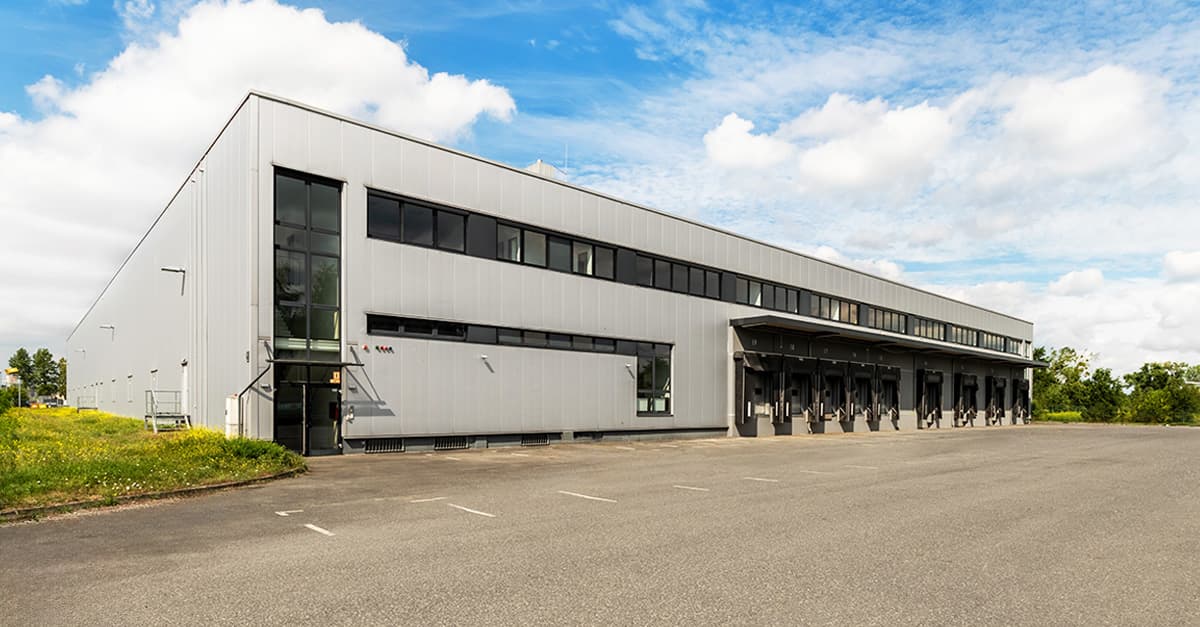 Large industrial warehouse with loading docks and parking area under a partly cloudy sky.
