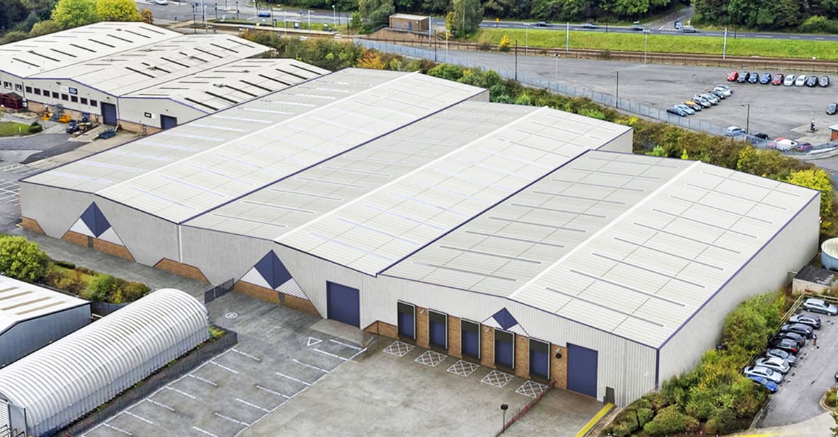 Aerial view of a large industrial warehouse complex with multiple connected buildings, adjacent parking lots, and surrounding greenery.