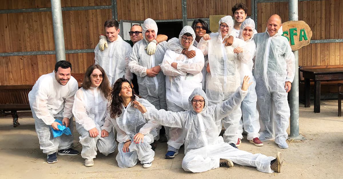 A group of people wearing white protective suits poses together outdoors in front of a wooden structure.