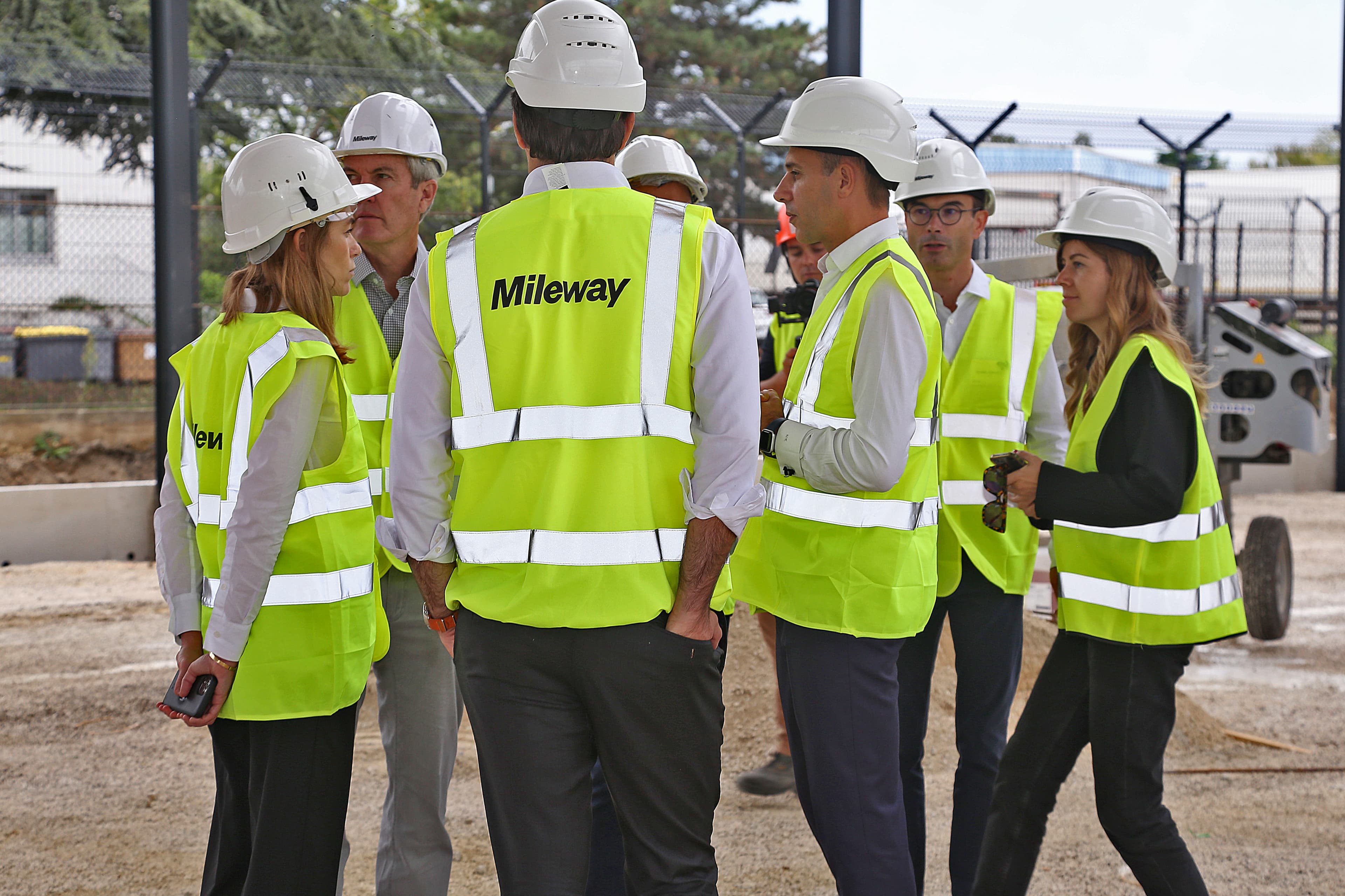 Group of people wearing high-visibility vests and hard hats, standing outdoors on a construction site.