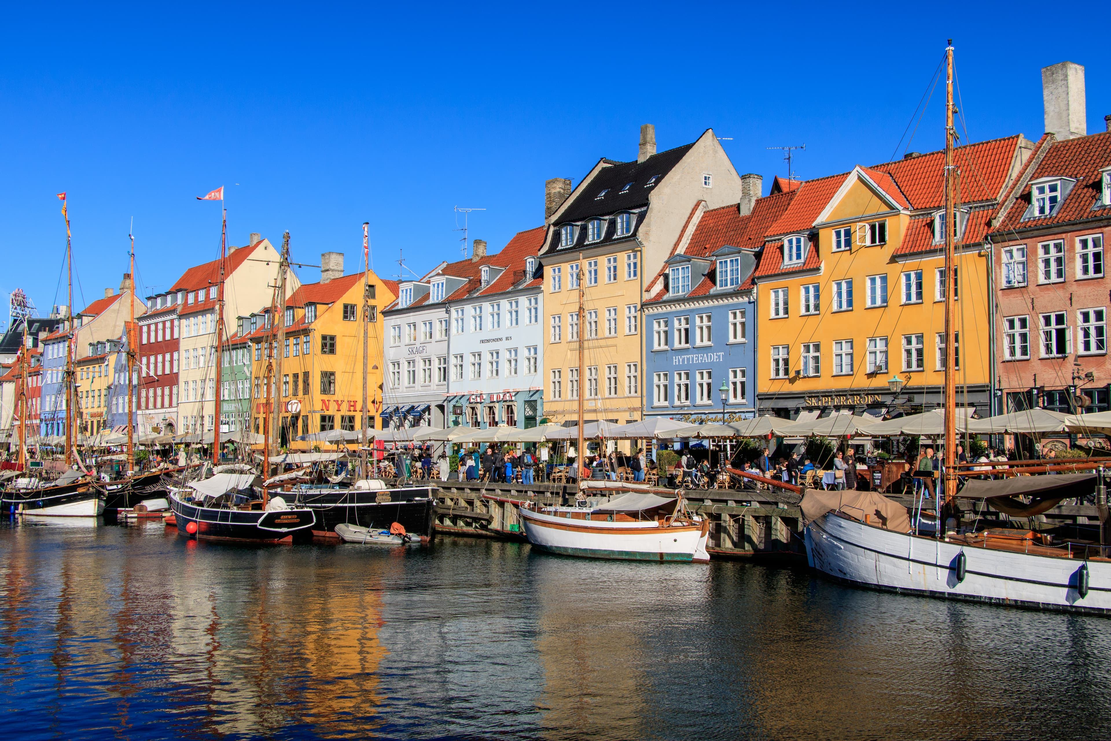 Colorful buildings line a waterfront with boats docked at the harbor under a clear blue sky.