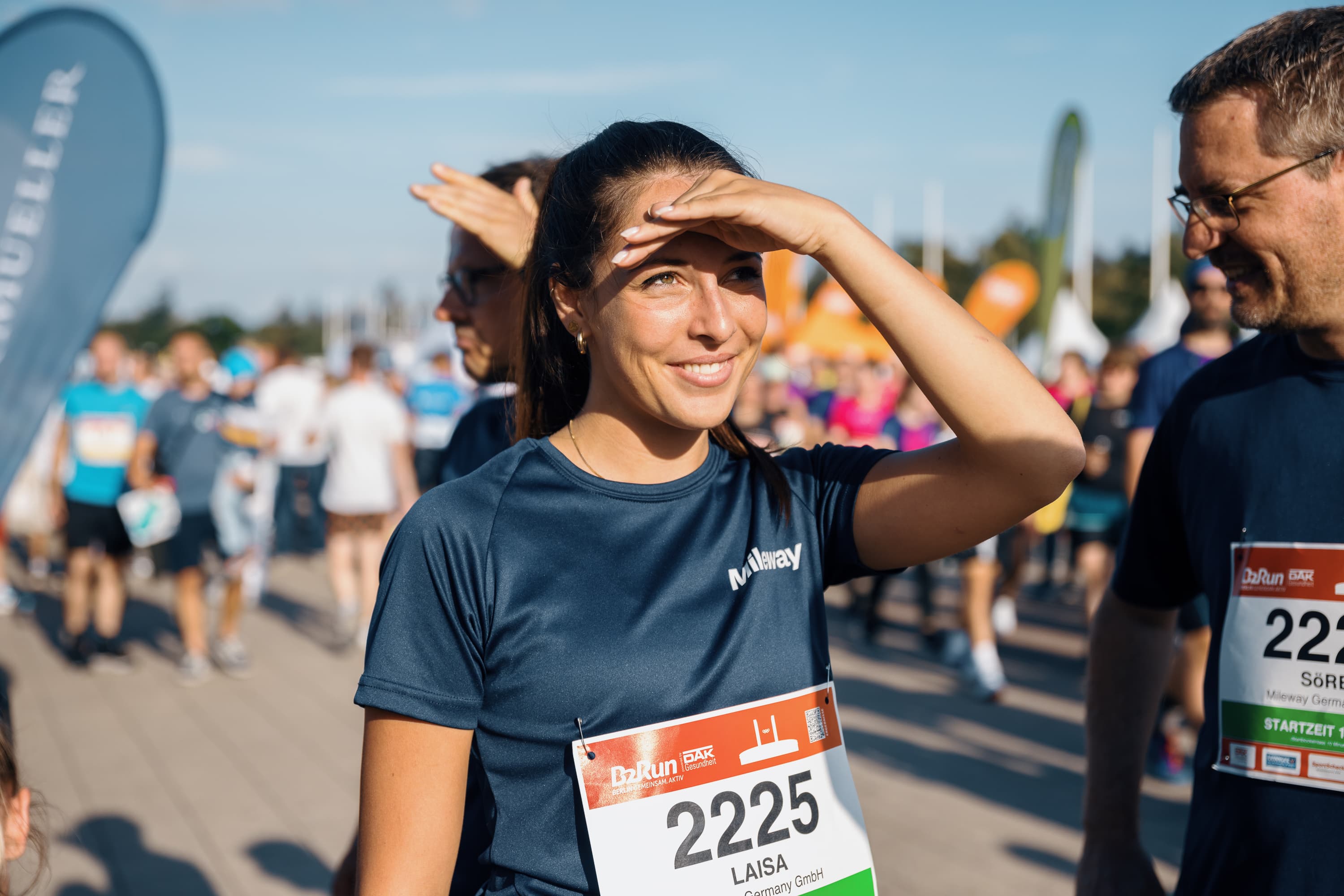 Woman shielding her eyes with her hand while participating in an outdoor race event, wearing a numbered bib.