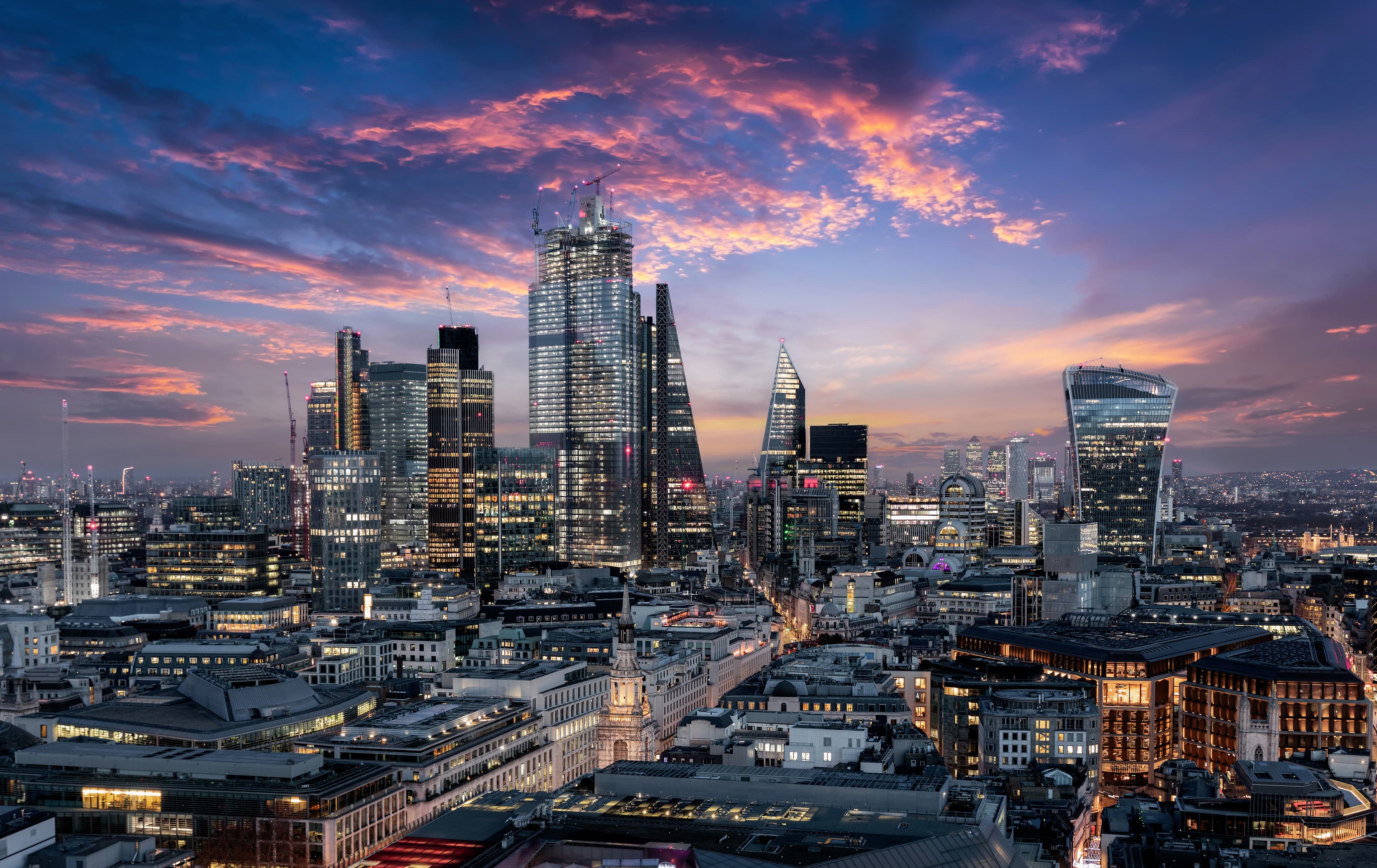 A cityscape of London at dusk, featuring modern skyscrapers and a colorful sky with scattered clouds.