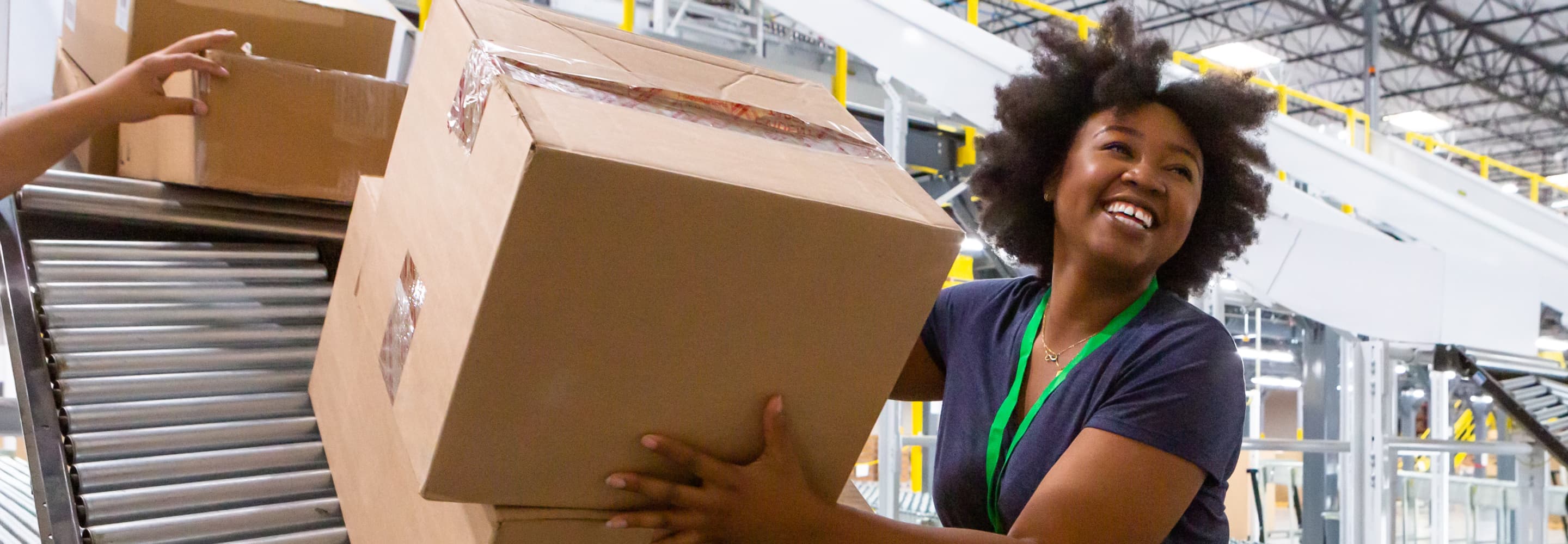 Person smiling while handling a large box on a conveyor belt in a warehouse setting.
