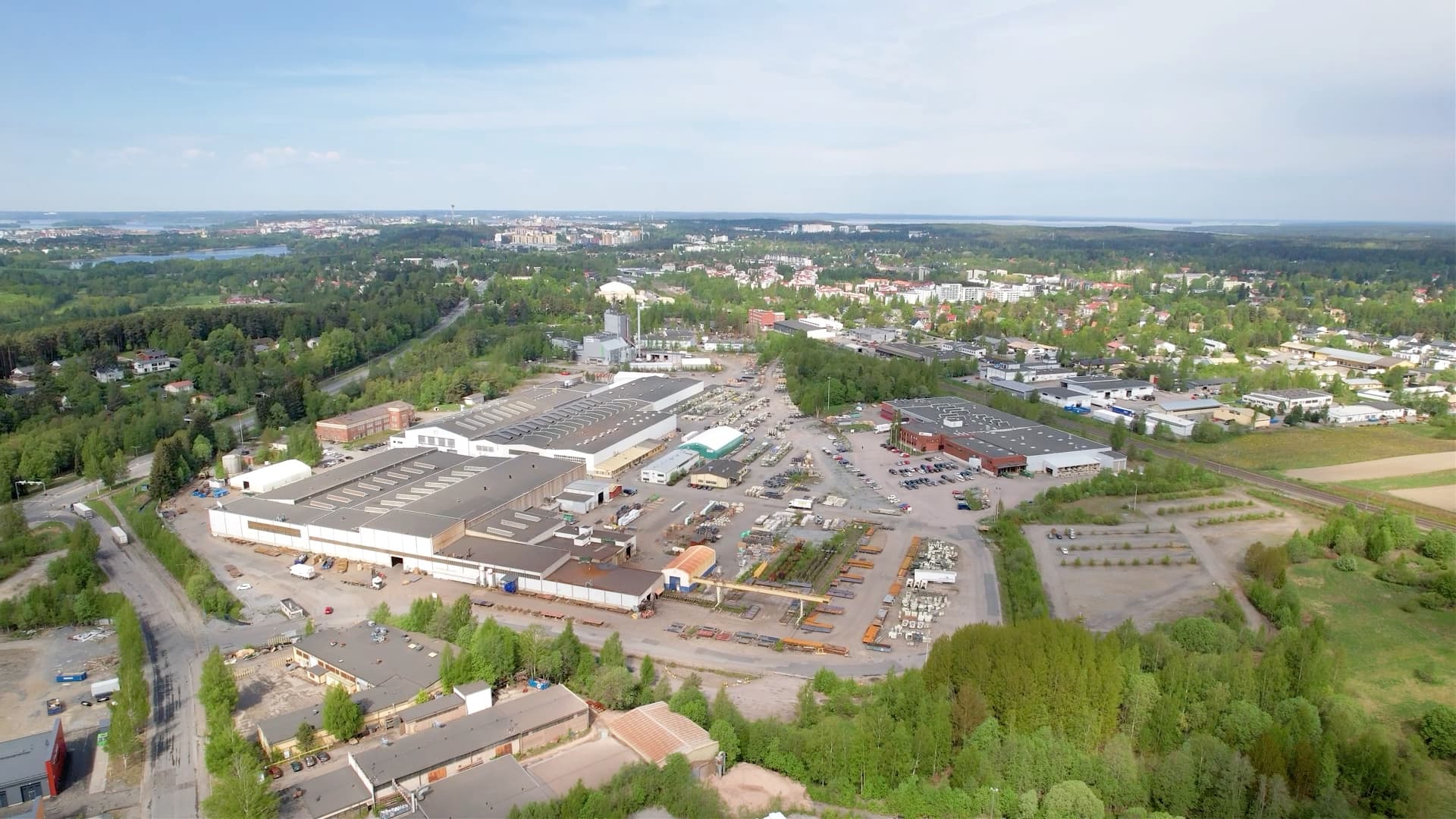 Aerial view of an industrial area surrounded by greenery and residential buildings under a clear blue sky.