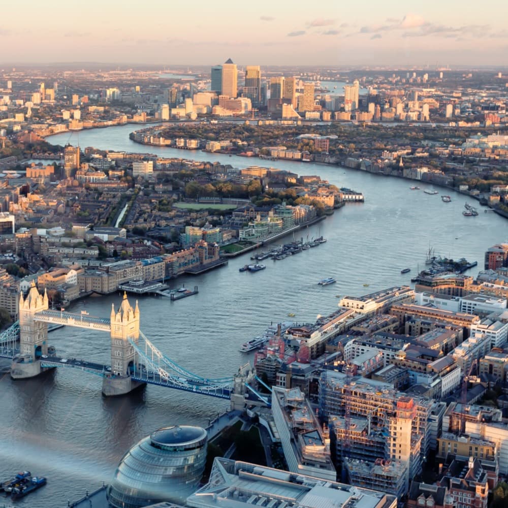 Aerial view of London at sunset, featuring the River Thames, Tower Bridge, and city buildings.