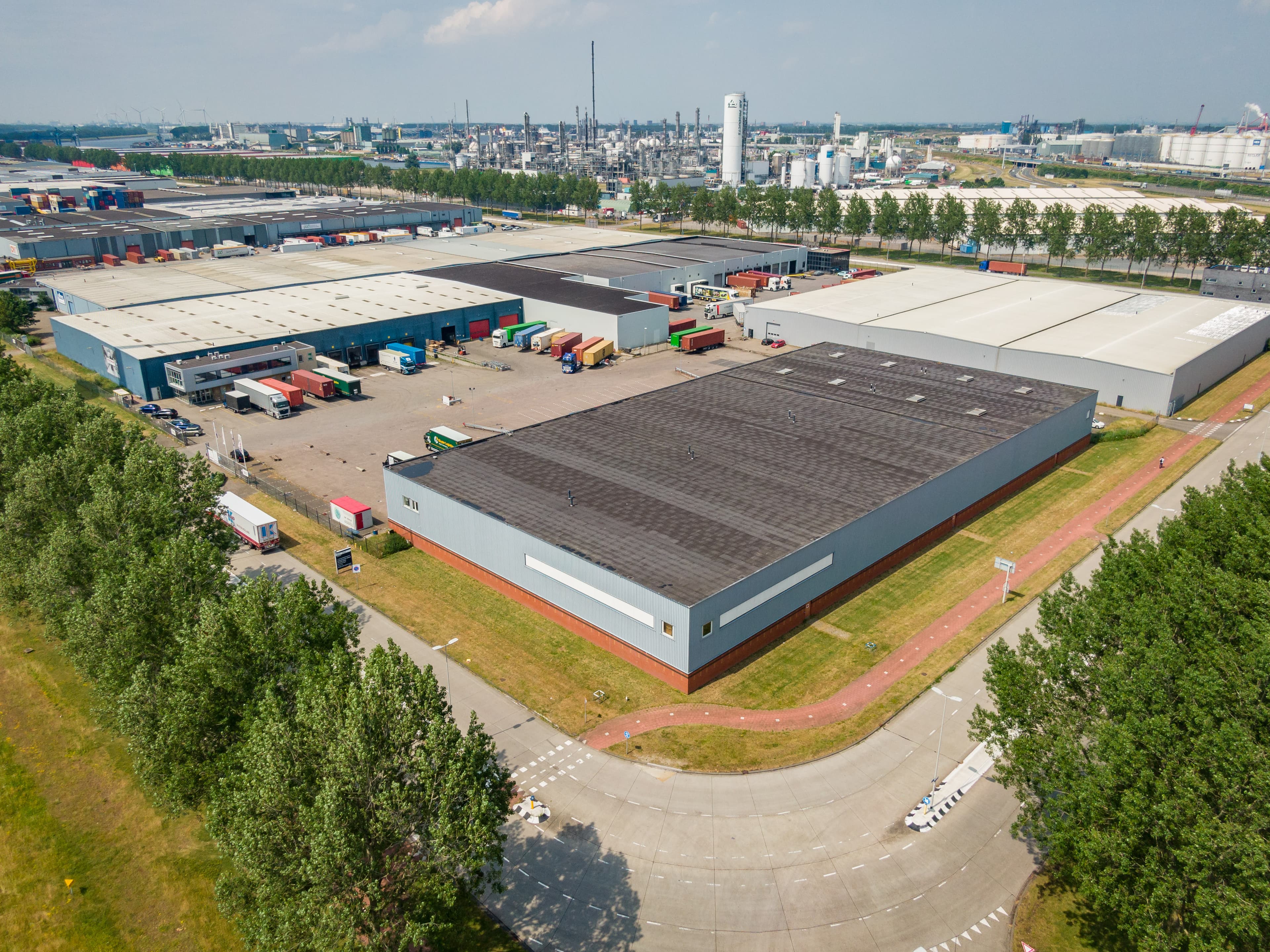Aerial view of an industrial warehouse complex with multiple large buildings, shipping containers, and surrounding trees on a clear day.