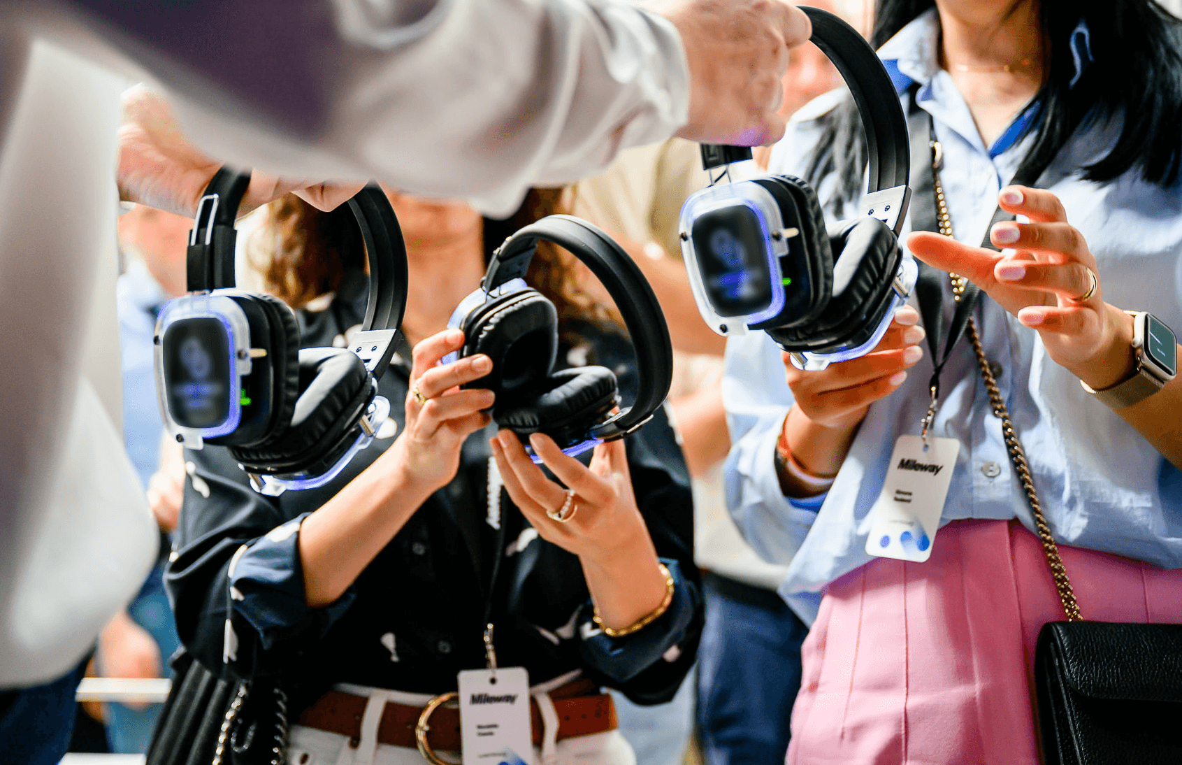 People holding LED headphones at an event, wearing lanyards.
