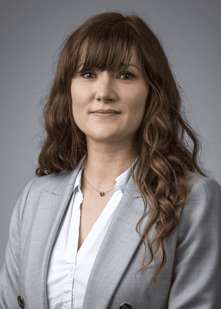 Person in a light gray blazer and white blouse, posing against a plain gray background.