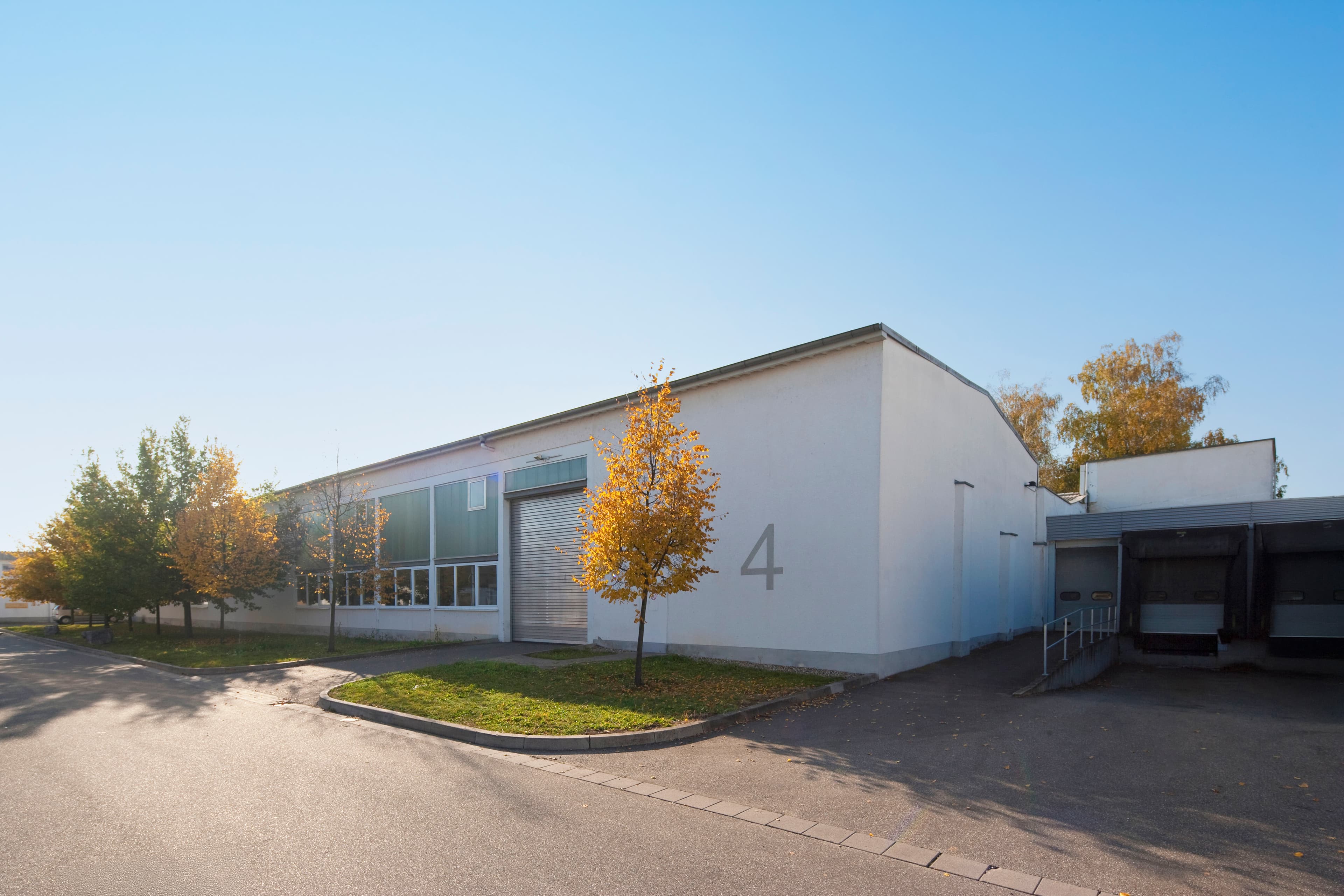 A white industrial building with a large number 4 on the side, surrounded by trees under a clear blue sky.