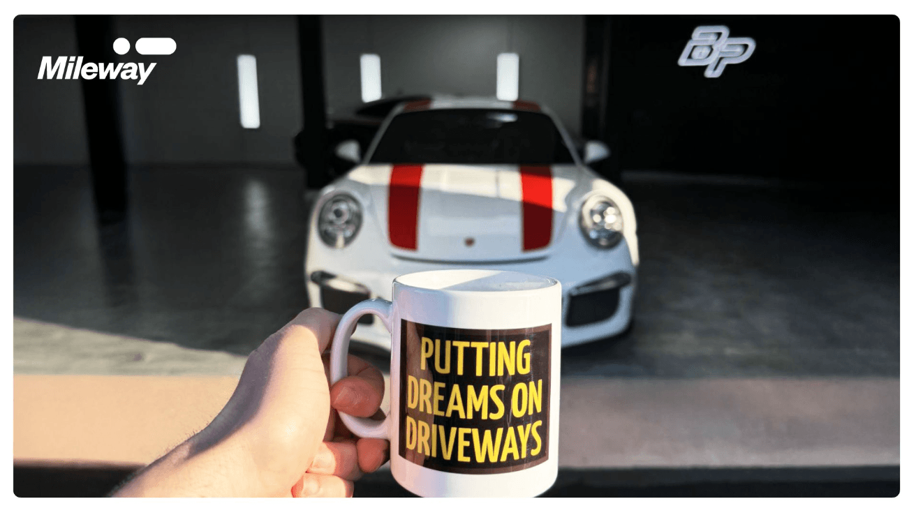 A person holds a mug with the text Putting Dreams on Driveways in front of a white sports car with red stripes.