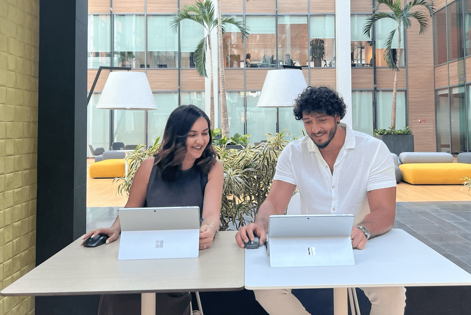 Två personer sitter vid varsitt bord på en modern innergård och arbetar på surfplattor med tangentbord och mus.