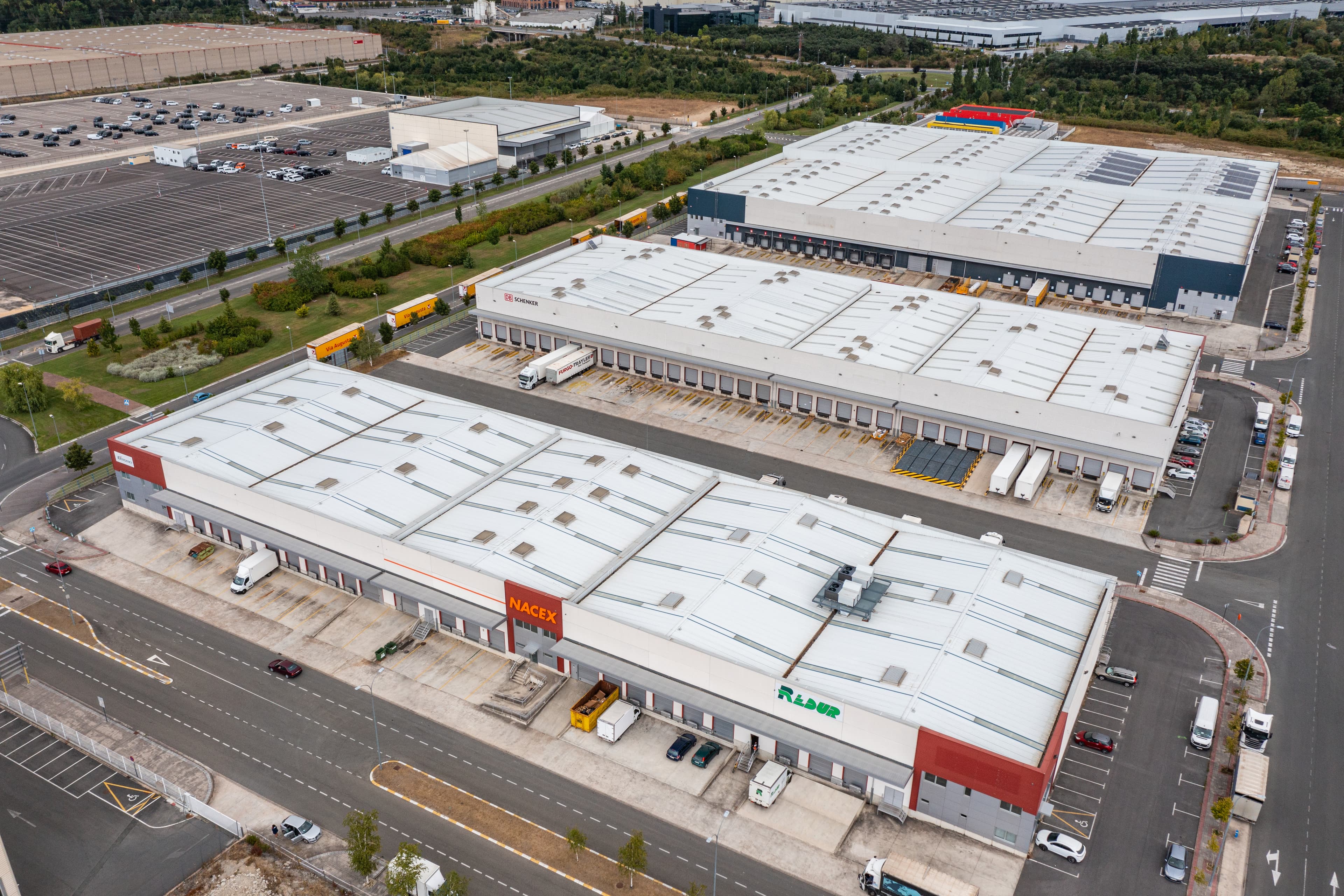 Aerial view of large industrial warehouses with loading bays, lorries, and car parks in a commercial area.